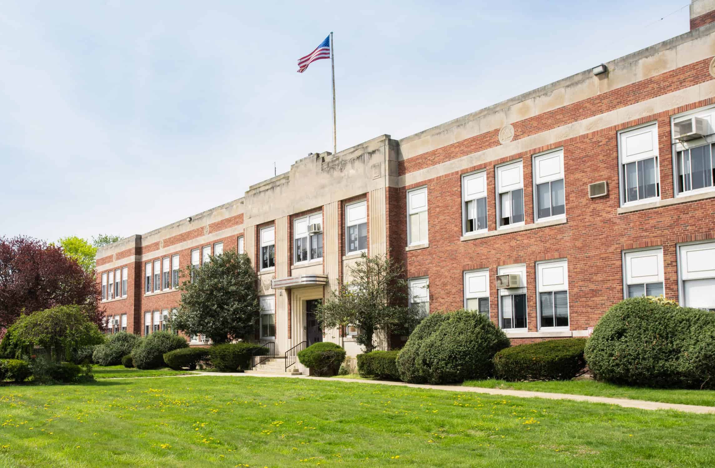 Exterior Commercial Painting for Schools and Institutions Classic red brick school building with white trim, American flag, and lush green lawn — commercial exterior painting Concord MA