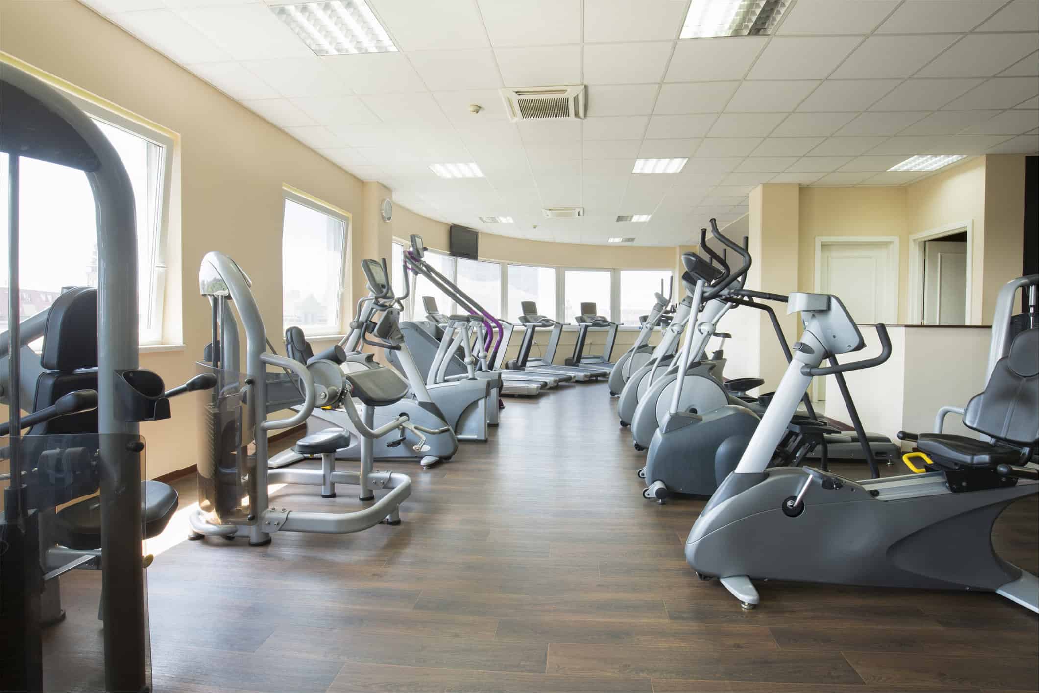 Gym & Fitness Center Interior Painting Clean gym interior with rows of grey cardio machines, peach painted walls, dark hardwood floor, and large curved windows