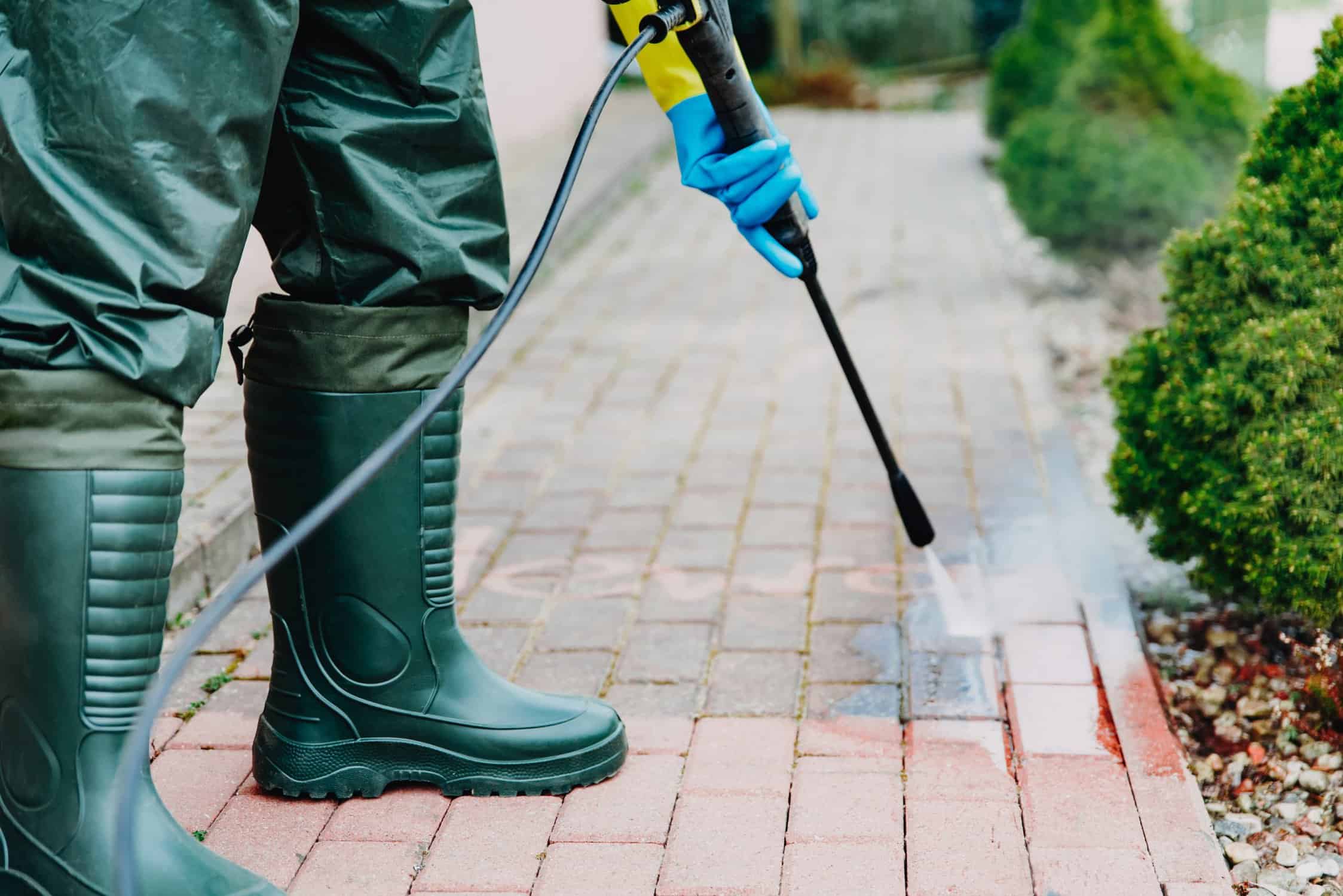 Man cleaning red, conrete pavement block using high pressure water cleaner. High pressure cleaning.