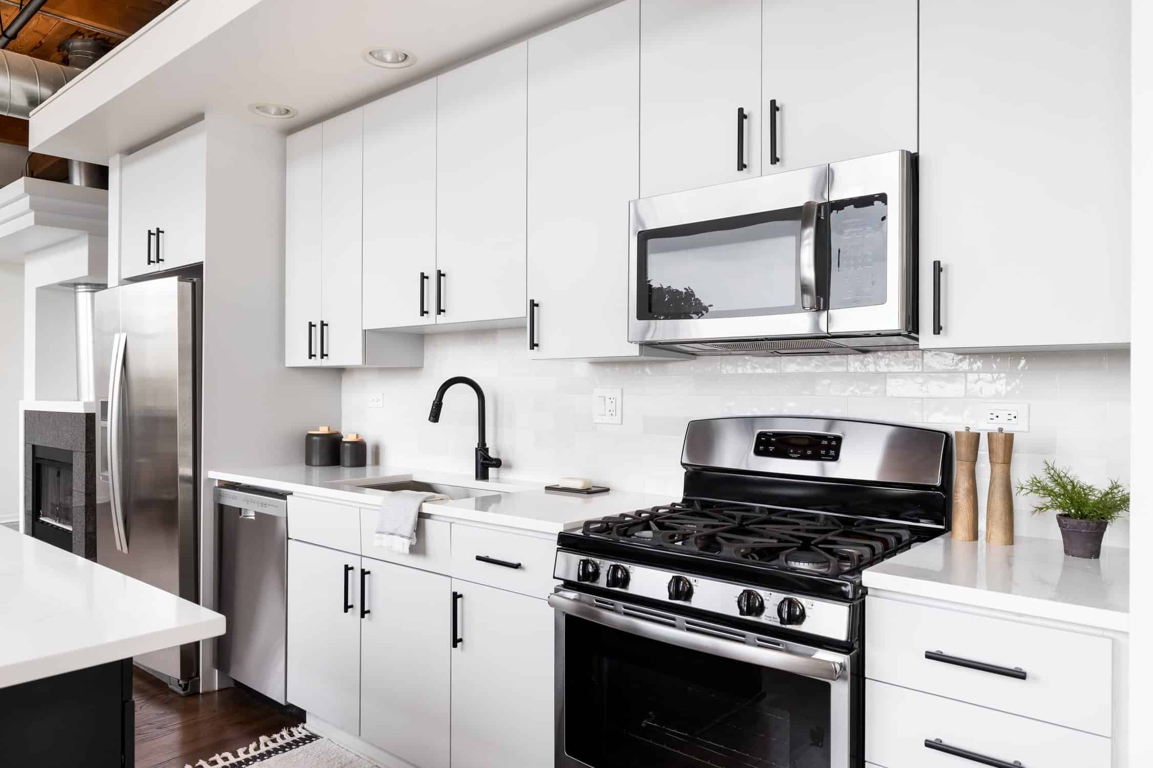 A loft kitchen with white cabinets, exposed wood ceiling, and stainless steel appliances.