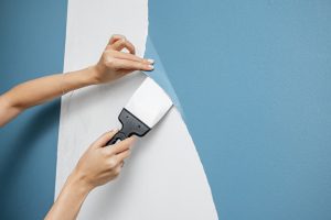 A Woman Housewife Peels Off An Old Vinyl Wallpaper With Scraper