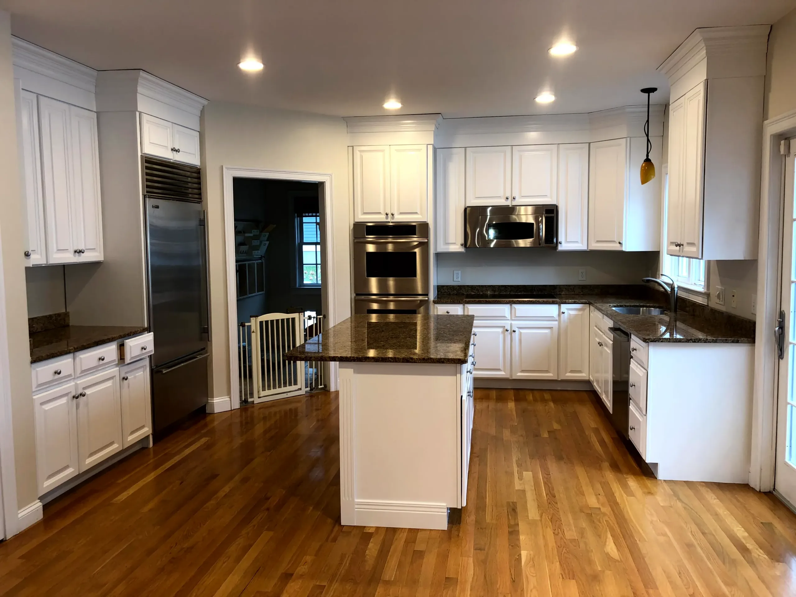 IMG_5116 A spacious, bright kitchen featuring freshly painted white cabinets, dark granite countertops, stainless steel appliances, and hardwood floors.